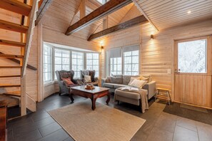 Interior de una cabaña de madera con escalera, paredes de madera, un sofá, un sillón y una mesa de centro.