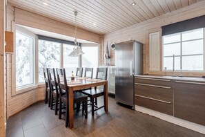 Una cocina con paneles de madera, una mesa de comedor y sillas, un refrigerador y ventanas grandes.
