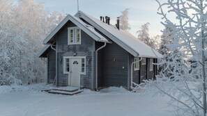 Una cabaña pequeña de un solo nivel con puerta principal, chimenea y techo cubierto de nieve.