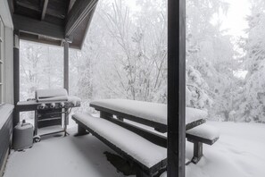 Un espacio al aire libre cubierto de nieve con un banco de madera y una parrilla.