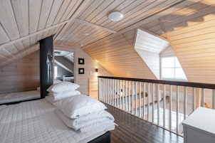 Un dormitorio con techo inclinado, una cama con ropa blanca, una ventana y una escalera que conduce a un nivel superior.