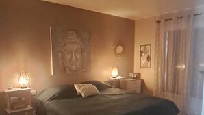Un dormitorio con una cama, mesitas de noche, una estatua de Buda, un reloj de pared y un cuadro.