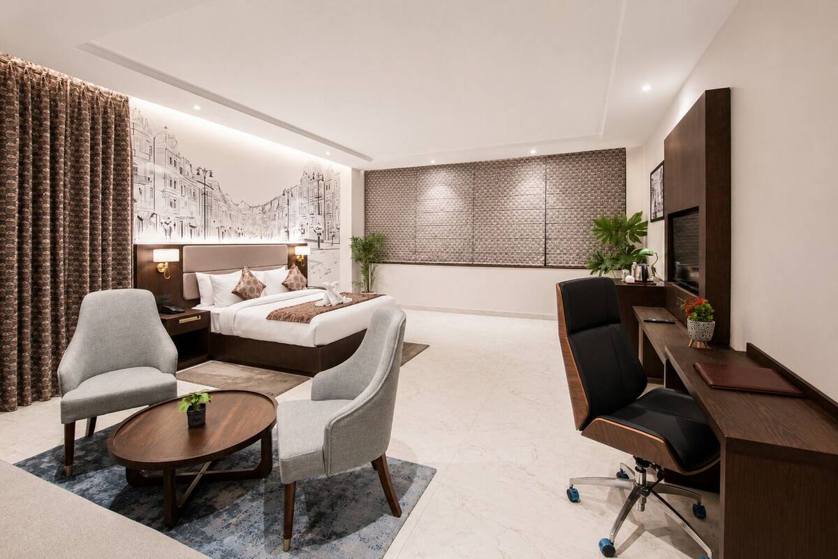 Una habitación de hotel moderna con cama, dos sillones, un escritorio y un mural grande en la pared.