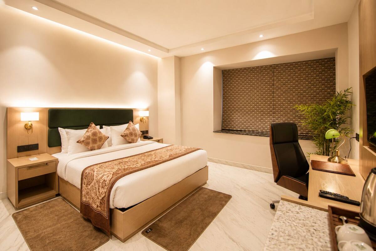 Habitación de hotel moderna con una cama grande, mesitas de noche, un escritorio, una silla, un televisor y una ventana con persiana estampada.