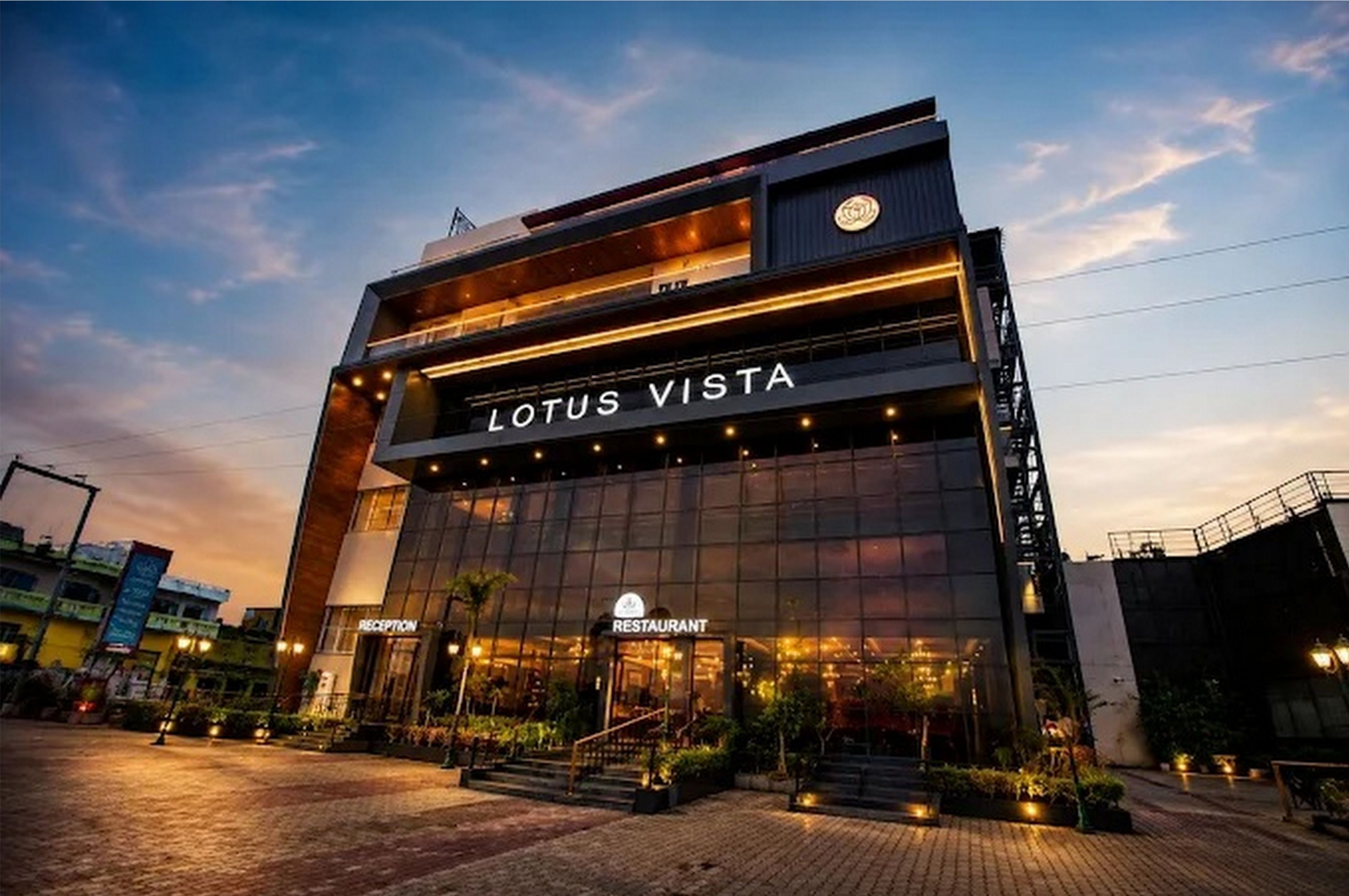 Un edificio moderno con letrero 'LOTUS VISTA', un área de recepción y la entrada a un restaurante.
