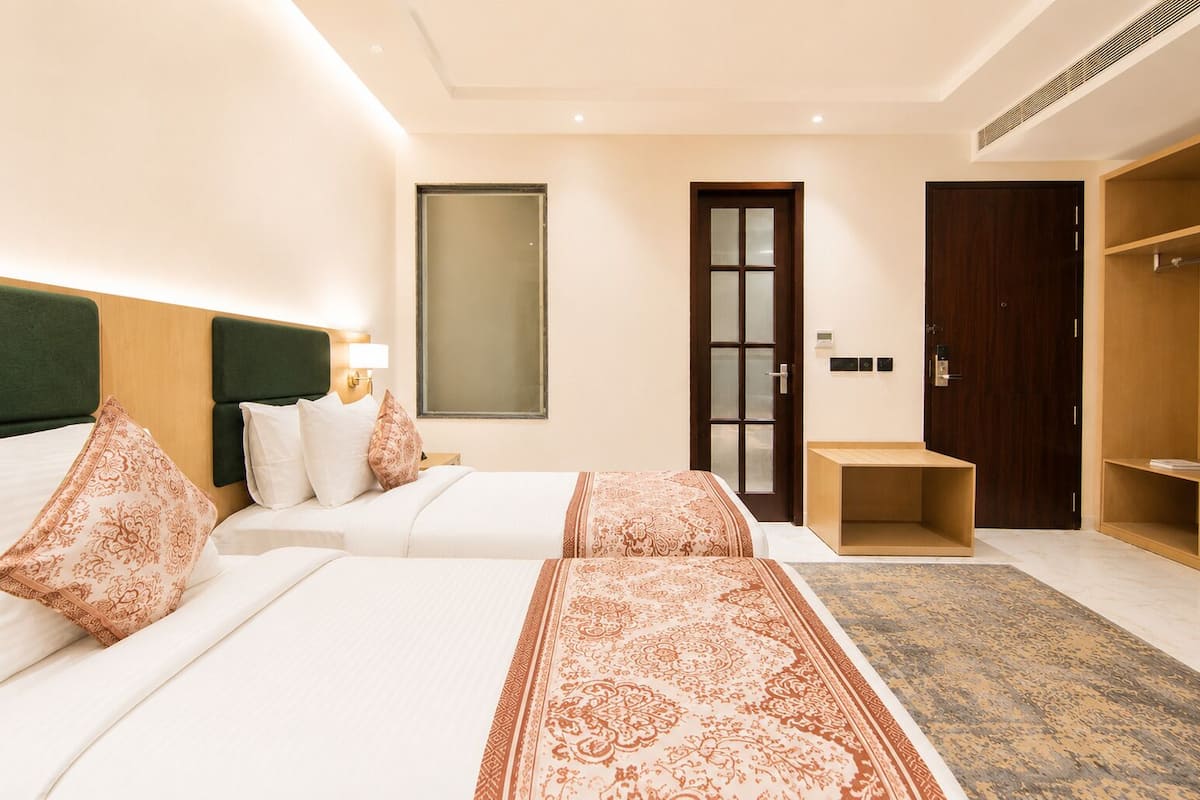 Una habitación de hotel con dos camas, un armario, una mesita y un espejo.