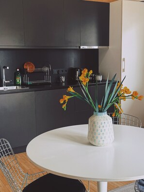 Eine moderne Küche mit dunklen Schränken, einem weißen Esstisch und einer Vase mit Blumen.