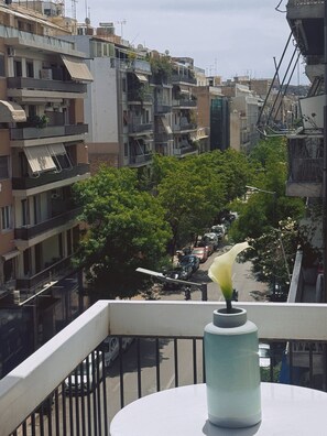 Ein Balkon mit Blumenvasen, mit Blick auf eine Straße mit parkenden Autos und Gebäuden.