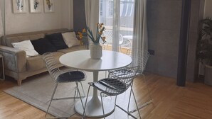 A modern living room with a sofa, a round dining table with chairs, a large window with curtains, and artwork on the wall. - Athens Acropolis View Balcony 2 Min to Metro (Athina)