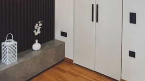 A modern room with a wooden floor, a dark wall with vertical lines, a white wardrobe with black handles, a white vase with flowers, and a hanging light fixture. - Athens Acropolis View Balcony 2 Min to Metro (Athina)