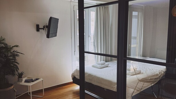 A room with a bed, a small table with a plant, a wall-mounted TV, and an air conditioning unit. - Athens Acropolis View Balcony 2 Min to Metro (Athina)