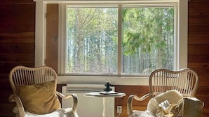 A room with two wicker chairs, a small table, and a large window with a view of trees.
