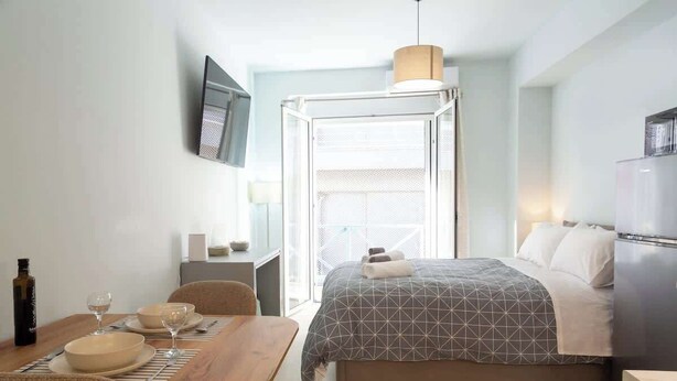 A hotel room with a bed, a desk, a chair, a dining table, and a TV mounted on the wall. - Studio 4 Kalamata - Bright Escape in the Centre (Kalamata)