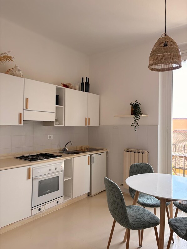 Une cuisine moderne avec des meubles blancs, une cuisinière à gaz, un four encastré, un évier et un coin repas comprenant une table ronde et quatre chaises.