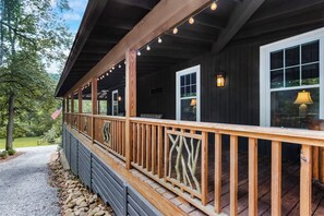 A wooden deck with a railing, a porch, and a window with a lamp.