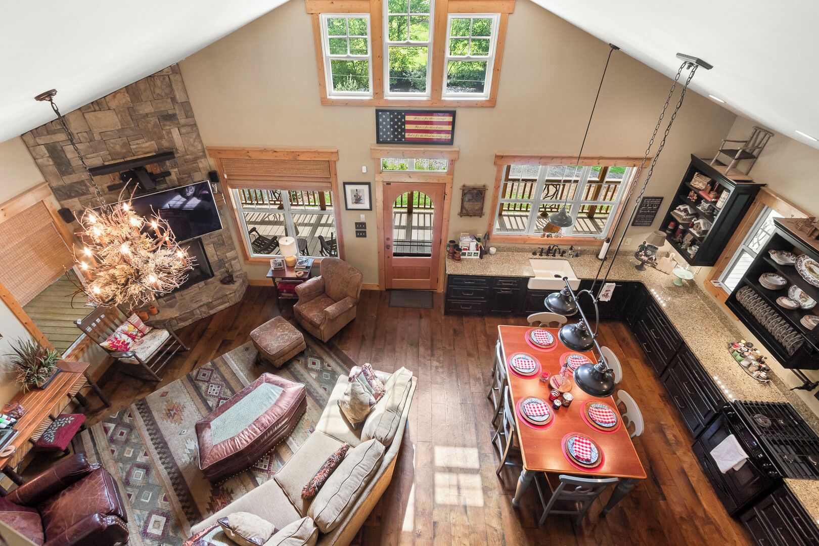A spacious loft with a dining area, kitchen, and living room, featuring a stone fireplace, wooden beams, and large windows.
