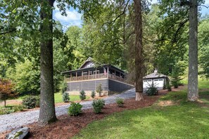 A cabin with a porch, surrounded by trees and a small shed.