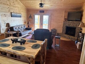 L'intérieur d'un chalet en bois comprend une table à manger, un canapé, une cheminée et un téléviseur.