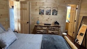 A wooden cabin bedroom with a bed, dresser, and artwork on the wall. - Cozy Wooded Retreat! (Murphy)