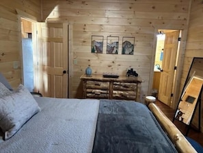 Ein Schlafzimmer einer Holzhütte mit Bett, Schminktisch und Bildern an der Wand.