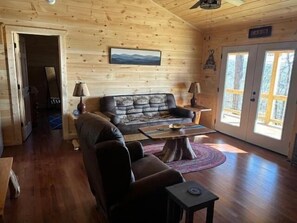 A wooden interior with a sofa, two lamps, a coffee table, and a door leading outside. - Cozy Wooded Retreat! (Murphy)