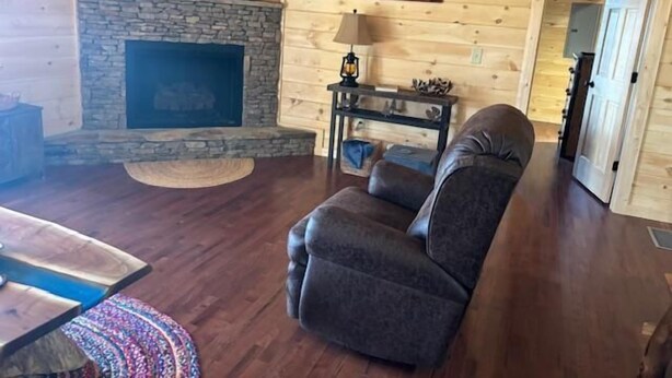 A log cabin interior with a stone fireplace, a leather sofa, and a television mounted above the fireplace. - Cozy Wooded Retreat! (Murphy)