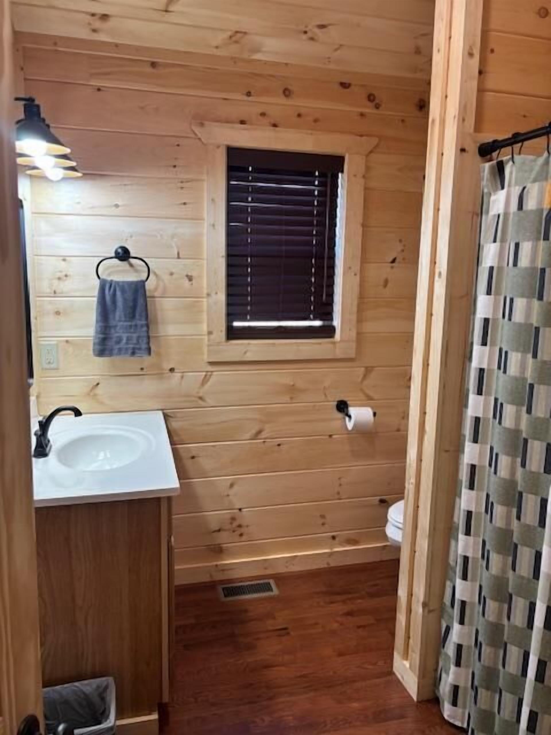 A wooden cabin bathroom with a sink, window, and shower curtain.