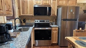 A kitchen with wooden cabinets, a stainless steel refrigerator, a microwave, an oven, and a sink. - Cozy Wooded Retreat! (Murphy)