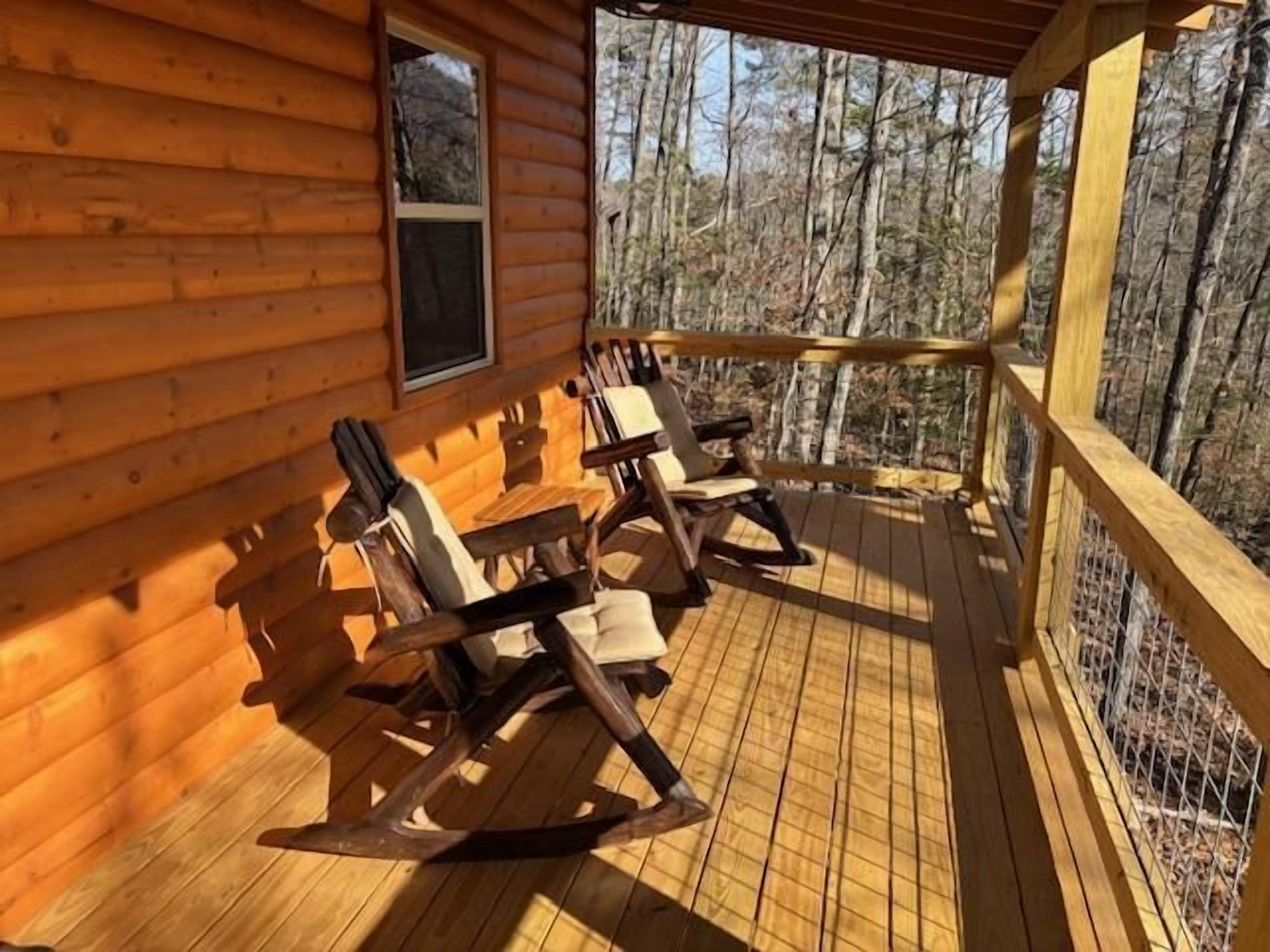 A wooden cabin with a porch, rocking chairs, and a window overlooking a forest.