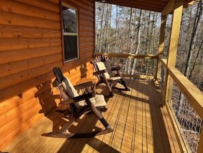 Eine Holzhütte mit Veranda, Schaukelstühlen und einem Fenster mit Blick auf einen Wald.