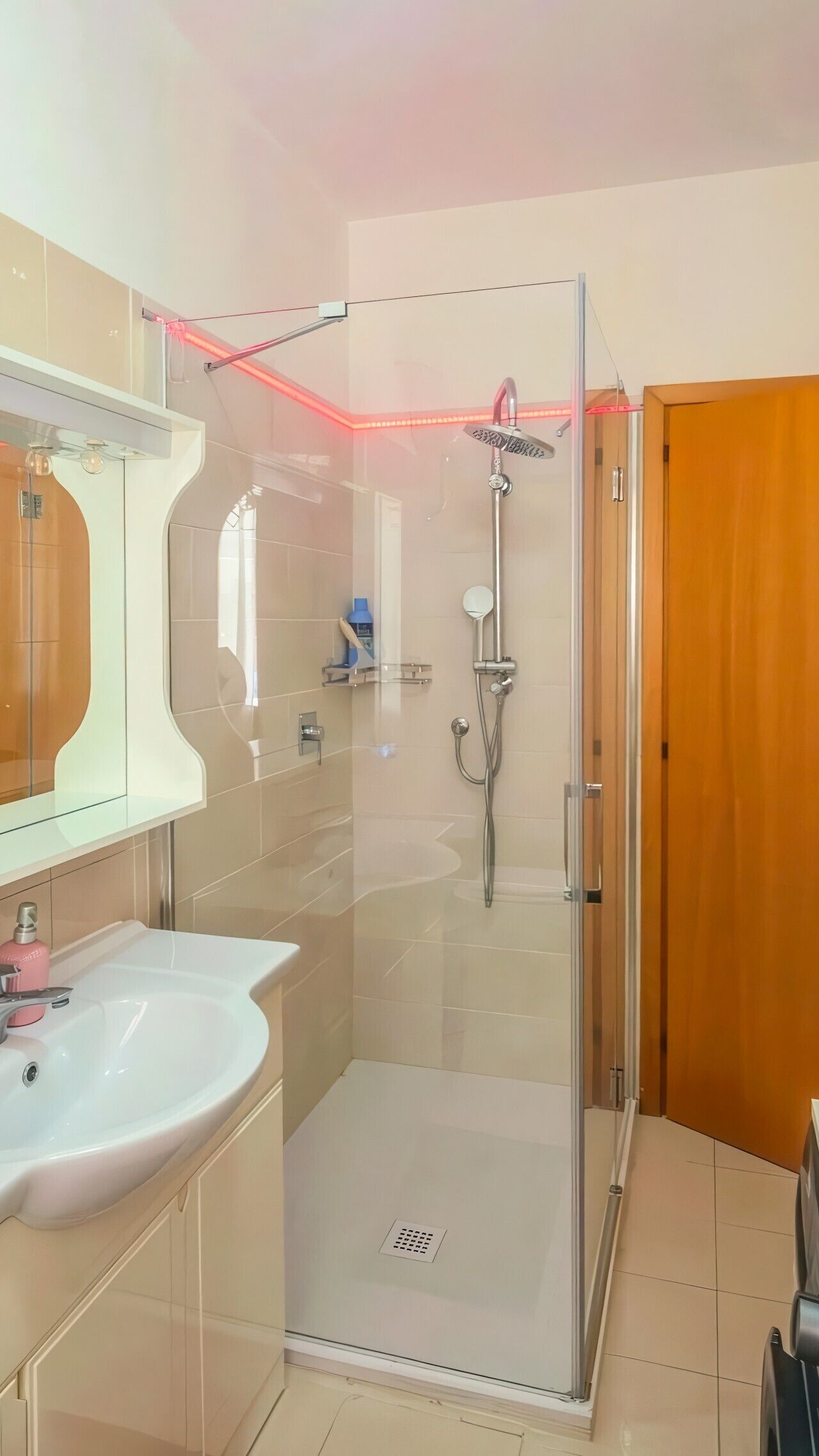 Une salle de bain moderne avec une douche à parois de verre, un lavabo blanc et une porte en bois.