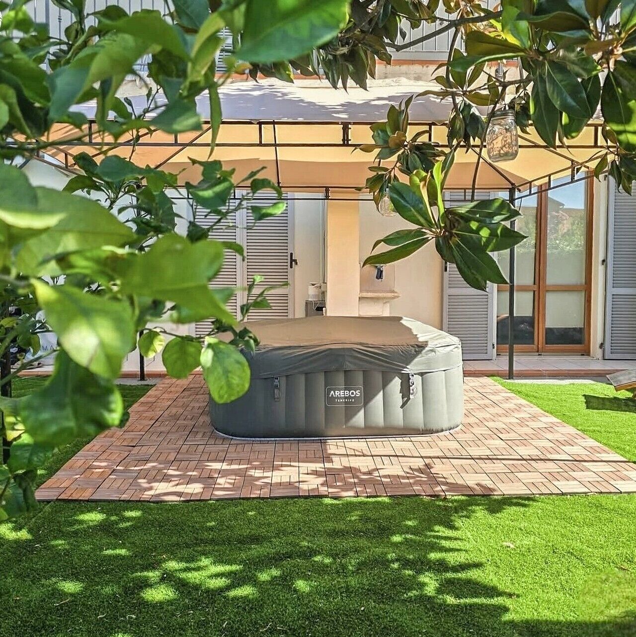 A modern outdoor seating area with a covered bench, a glass door entrance, and a well-maintained lawn.