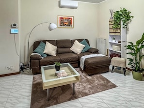A living room with a brown sofa, a glass coffee table, a lamp, a radiator, and a bookshelf with plants. - Villa Garden - Porto San Giorgio (Porto San Giorgio)