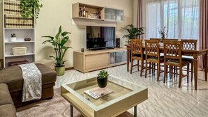 Una sala de estar con sofá, una mesa de centro de vidrio, televisor, estantería y comedor con sillas.