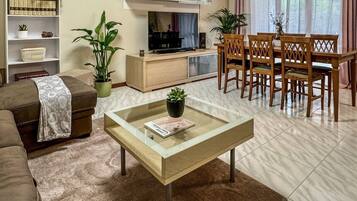 Un salon comprenant un canapé, une table basse en verre, un téléviseur, une bibliothèque et un coin repas avec des chaises.