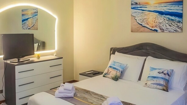 Un dormitorio con cama, mesitas de noche, televisor y cuadros en la pared.