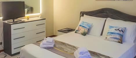 Un dormitorio con cama, mesitas de noche, televisor y cuadros en la pared.