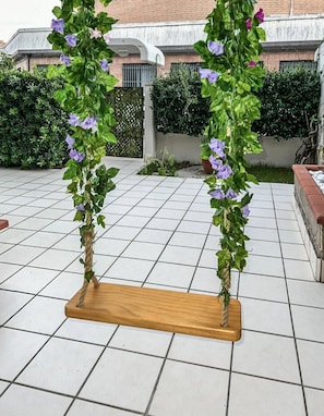 A wooden swing with a rope, surrounded by a tiled patio area. - Villa Garden - Porto San Giorgio (Porto San Giorgio)