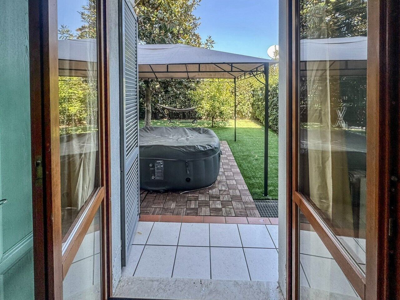 Un espacio de estar al aire libre cubierto con un jacuzzi, una hamaca y un patio con suelo de baldosas.