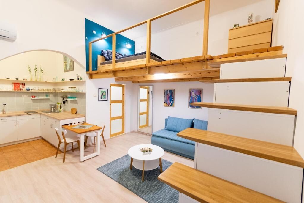 Un espace de vie compact comprenant une kitchenette, un coin repas, un canapé et une chambre en mezzanine avec un lit.