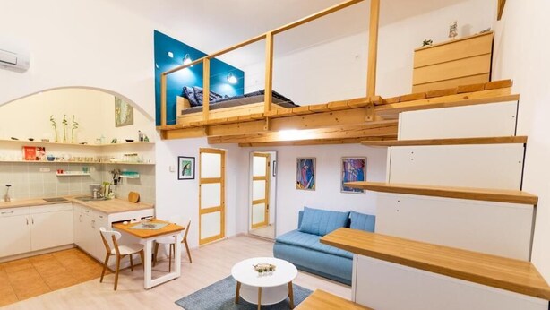 Ein kompakter Wohnraum mit Küchenzeile, Essbereich, Sofa und Schlafgalerie mit Bett.