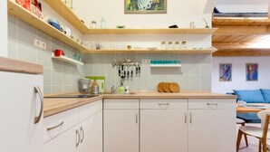 Eine Küche mit weißen Schränken, Holz Arbeitsplatten und einer gefliesten Spritzschutzleiste. Über der Spüle befinden sich Regale mit verschiedenen Gegenständen, und an der Wand hängt ein Bild.