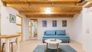 Ein Zimmer mit Holzboden, einem blauen Sofa, einem weißen Tisch und Kunstwerken an den Wänden.