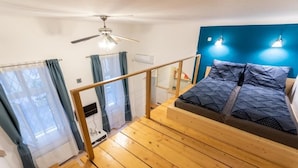 Ein Schlafzimmer mit Holzboden, einem Bett mit gemusterten Betttextilien, einem Deckenventilator und einer blauen Akzentwand.