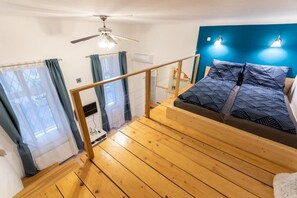 A bedroom with a wooden floor, a bed with patterned bedding, a ceiling fan, and a blue accent wall. - Blue & Wood Loft Stay in Budapest Soul (Budapest)