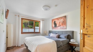Een slaapkamer met een bed, een raam, een schilderij en een houten deur.