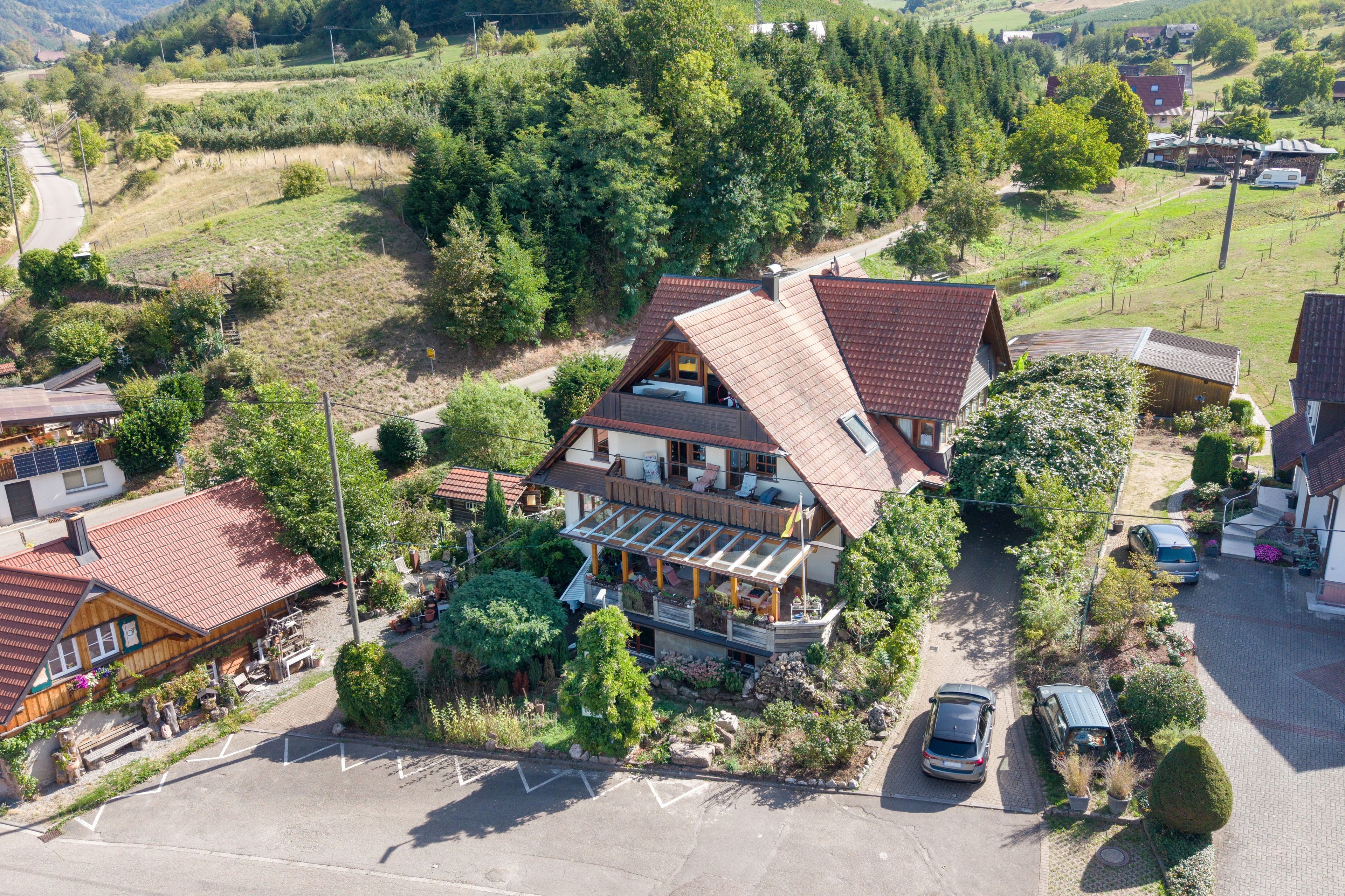 Ein zweistöckiges Haus mit geneigtem Dach, einer überdachten Terrasse und einem Parkplatz.