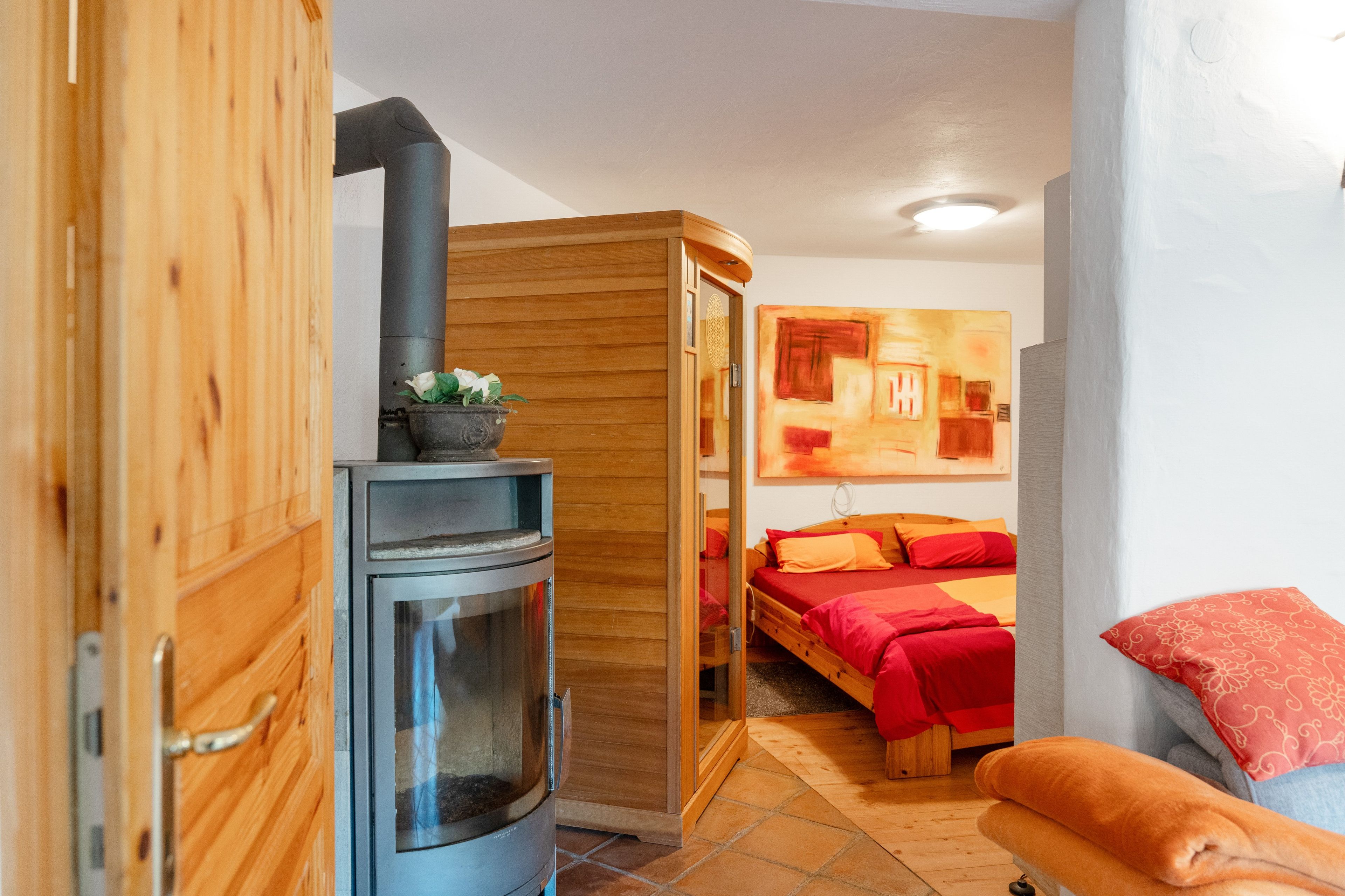 Une pièce de taille modeste, dotée d’un poêle à bois, d’un lit avec une literie rouge et d’un petit coin salon.