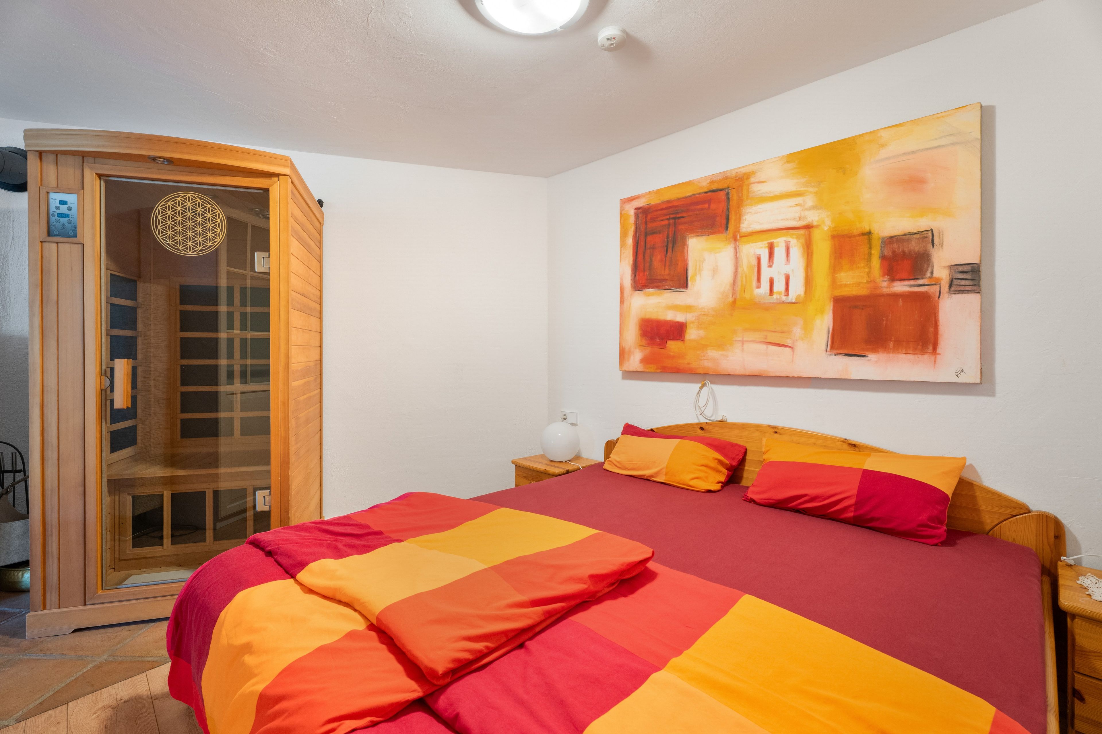 Ein Schlafzimmer mit einem Bett, einem Holzschrank, einem Wandbild und einer Deckenleuchte.