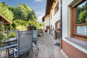 Un patio con mesa y sillas, rodeado de plantas en macetas y una pérgola de madera.
